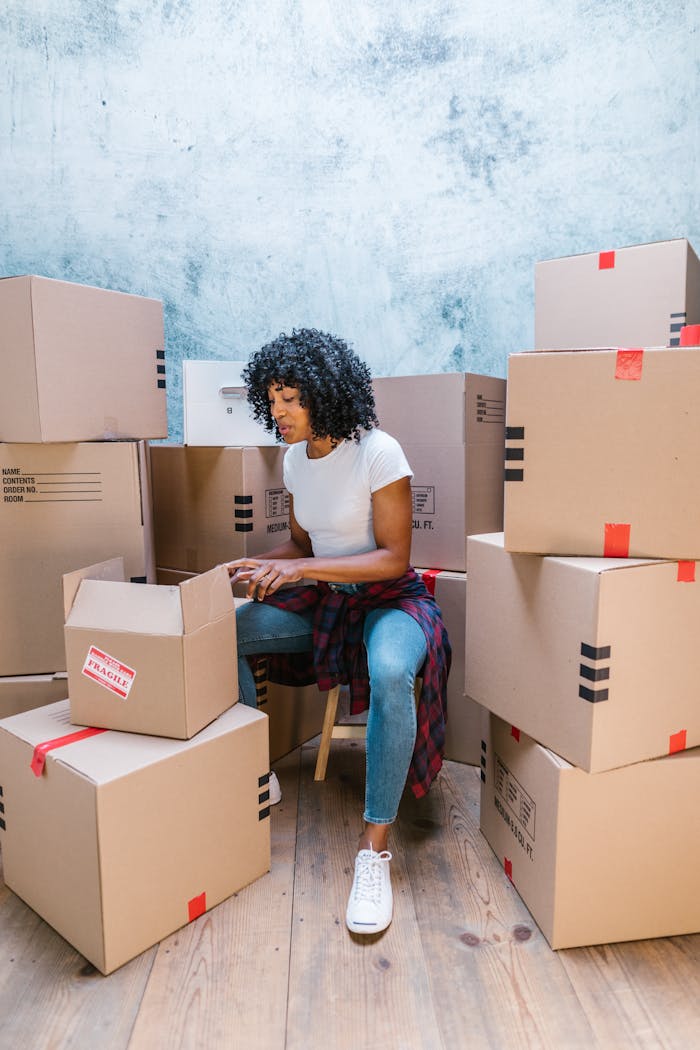 who-we-are A woman organizing cardboard boxes in a blue-toned room, preparing for a move.